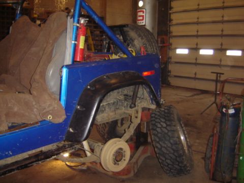 1992 Ford Bronco - The rear section of a modified blue off-road vehicle is shown in a garage setting, possibly undergoing repairs.