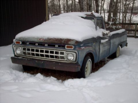 1965 Ford F-100 - A vintage pickup truck sits covered in snow, its front end partially visible.