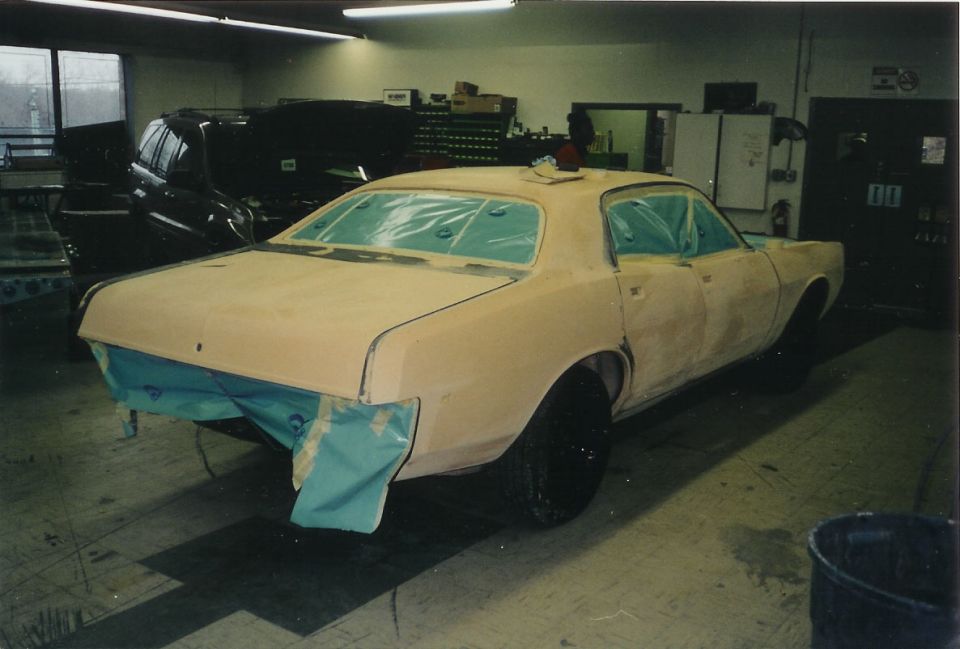 Tan primer coupe in body shop with masked windows, rear 3q view
