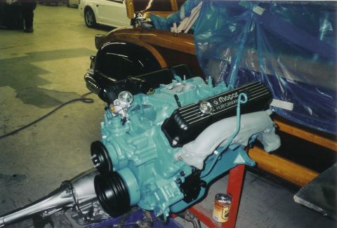 1978 Dodge Monaco - A turquoise Mopar engine and transmission assembly is displayed in a garage, with a woody car partially visible.
