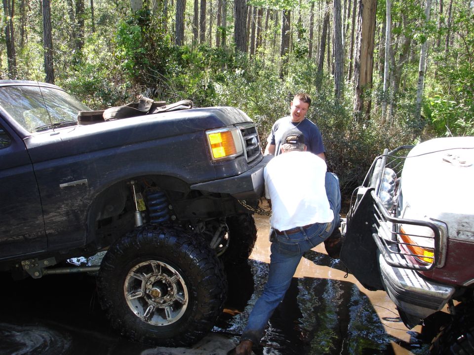 Dark blue lifted truck stuck in mud, front quarter view. Two men are near the front bumper