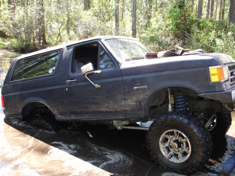 1989 Ford Bronco - This lifted Ford Bronco is navigating a water crossing in a wooded environment.