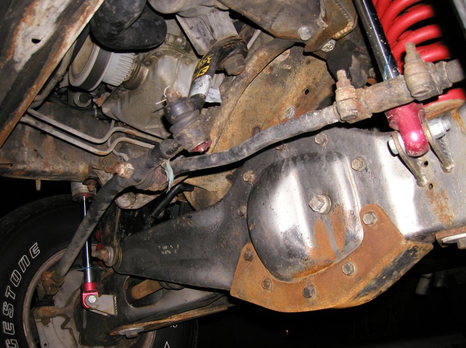 Underside of a solid front axle with differential cover, tie rod and red coilover shock