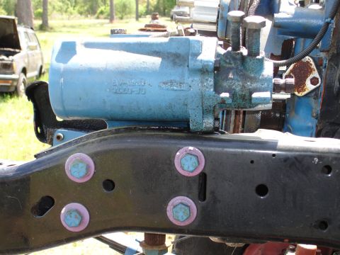 1989 Ford Bronco - A blue hydraulic pump assembly is attached to a black frame, with a partially visible vehicle in the background.