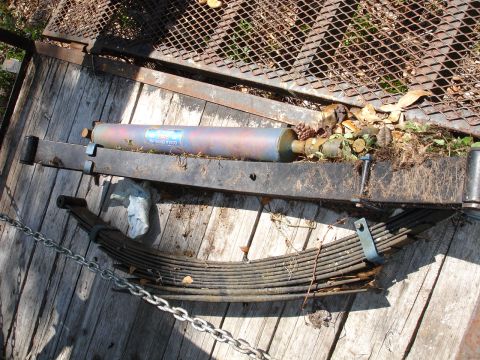 1989 Ford Bronco - Vehicle suspension parts, including leaf springs and a shock absorber, are laid out on a wooden deck.