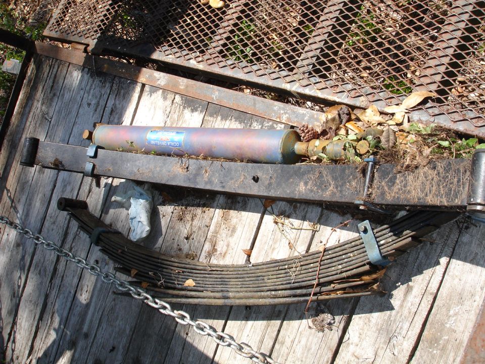 Leaf springs and a shock absorber are on a wooden surface, possibly a trailer