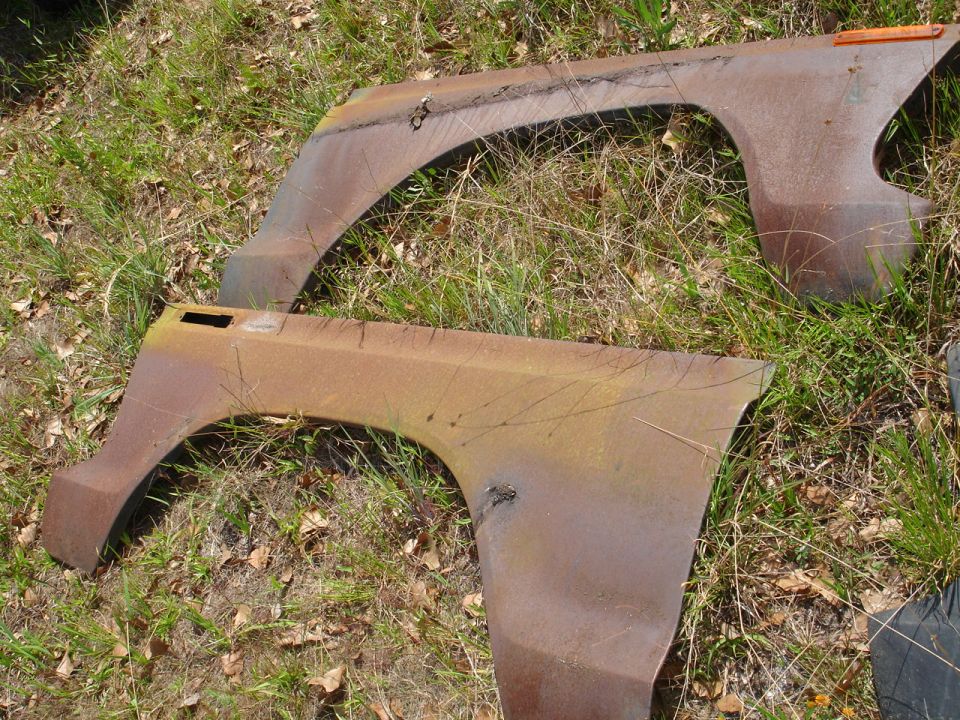 Two rusty, weathered fenders lying on the ground