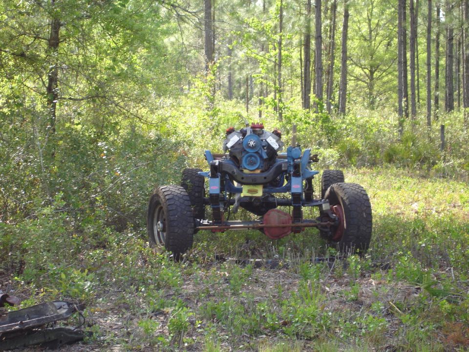 Off-road chassis with engine mounted, tires, and suspension components, in a wooded area