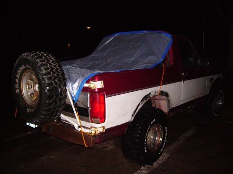 2000 Chevrolet Tahoe - A red and white pickup truck is viewed from the rear at night, with a tarp covering the bed and a spare tire mounted externally.