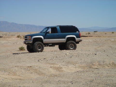 1988 Ford Bronco - This lifted SUV with off-road tires is parked in a dry, desert landscape under a clear blue sky.