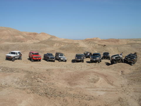 1988 Ford Bronco - Several off-road vehicles are gathered in a desert terrain under a clear blue sky.