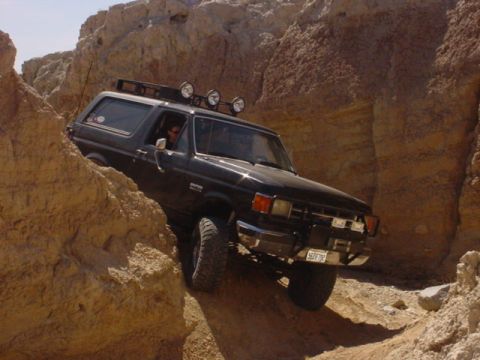 1988 Ford Bronco - This black Ford Bronco is navigating a challenging rocky terrain, with auxiliary lights mounted on its roof rack.