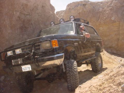 1988 Ford Bronco - This 1988 Ford Bronco is shown tackling a challenging off-road trail, equipped with auxiliary lights and a roof rack.