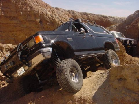 1988 Ford Bronco - This modified SUV is navigating a challenging off-road course with another vehicle in the background.