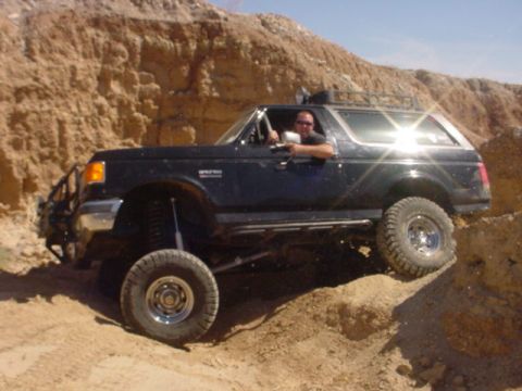 1988 Ford Bronco - A black 1988 Ford Bronco navigates a challenging off-road course with steep dirt inclines.