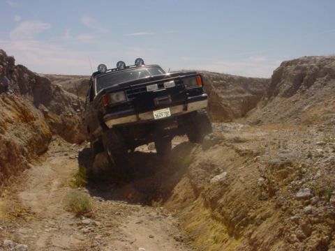 1988 Ford Bronco - 1988 Ford Bronco navigating a challenging off-road trail in a desert canyon.