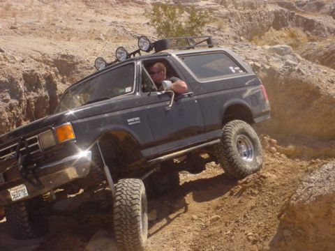 1988 Ford Bronco - A dark gray Ford Bronco navigates a challenging rocky terrain, demonstrating its off-road capabilities.