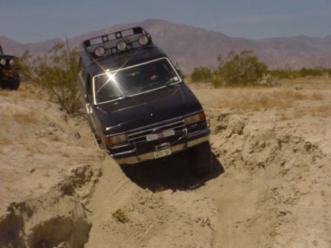 1988 Ford Bronco - A black Ford Bronco navigates a challenging off-road terrain, tilted precariously in a dirt ravine.