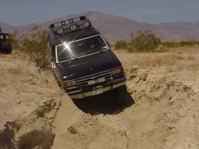Black Ford Bronco with roof lights driving off-road, tilted in a dirt ditch