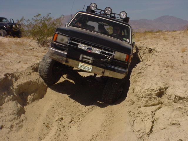 Black 1988 Ford Bronco navigating a steep dirt incline with another vehicle visible in the background