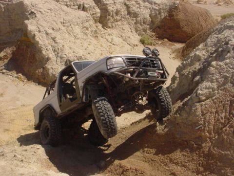 1988 Ford Bronco - Modified 1988 Ford Bronco tackling a challenging off-road trail in a rocky, desert-like environment.