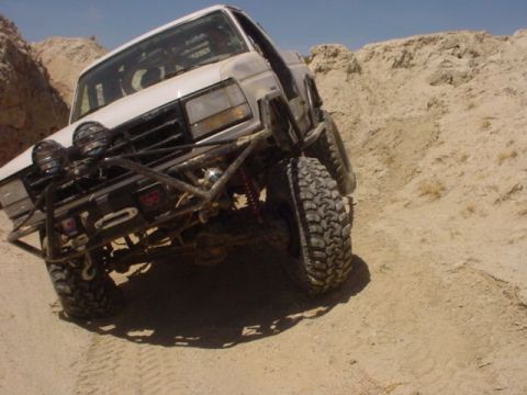 1988 Ford Bronco - This modified 1988 Ford Bronco navigates a challenging off-road terrain under a clear blue sky.