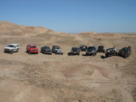 1988 Ford Bronco - Several off-road vehicles are gathered in a desert terrain under a clear blue sky.