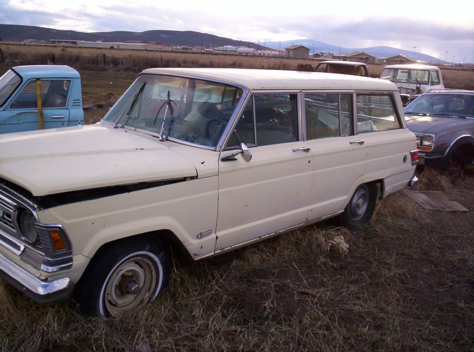 Tan Jeep Wagoneer full-size wagon parked in a dry field with damaged front fender among other vehicles