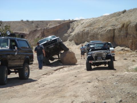 1988 Ford Bronco - Two Ford Broncos navigate a rocky off-road trail, with one vehicle attempting to ascend a large boulder.