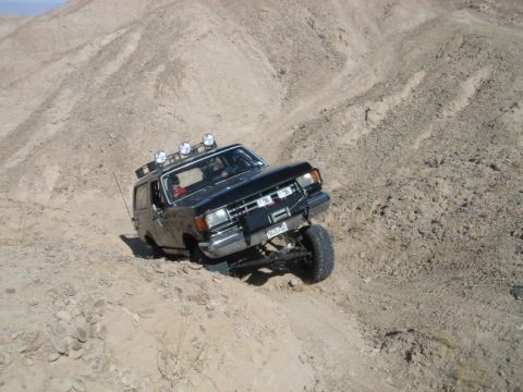 1988 Ford Bronco - This SUV is navigating a challenging off-road terrain with steep inclines and loose dirt.