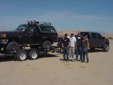 1988 Ford Bronco - A black Ford Bronco is loaded onto a trailer, with a dark gray Ford F-250 Super Duty parked behind it and four men standing in front of the…
