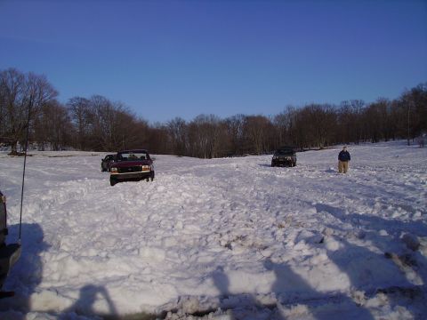 2000 Chevrolet Tahoe - A red pickup truck navigates a snow-covered field, with another vehicle and a person in the distance.