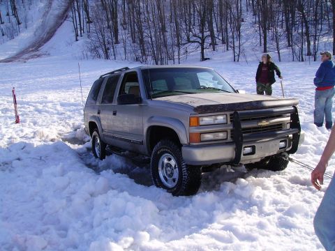 2000 Chevrolet Tahoe - Silver Chevrolet Tahoe stuck in snow with people nearby.