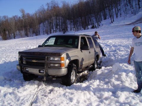 2000 Chevrolet Tahoe - A Chevrolet Suburban is stuck in the snow with two people attempting to free it.