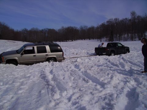 2000 Chevrolet Tahoe - A tan SUV is being towed by a dark pickup truck through a snow-covered field.