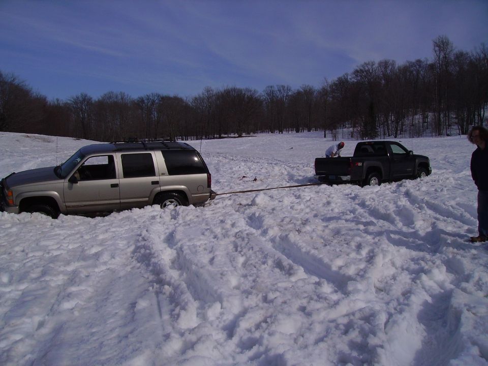 Tan SUV stuck in snow, being towed by dark pickup truck