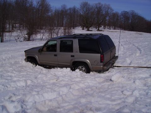 2000 Chevrolet Tahoe - SUV buried in snowdrift with trees in background.