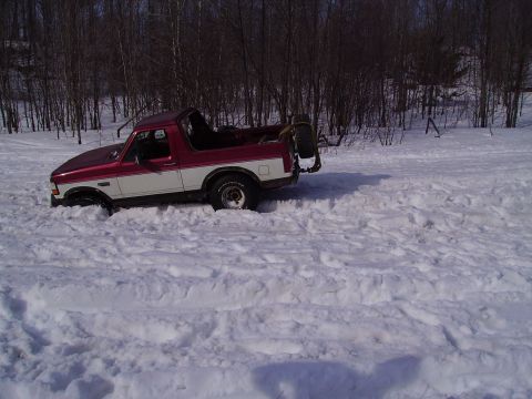 2000 Chevrolet Tahoe - A two-tone Ford Bronco is partially buried in snow, with trees in the background.
