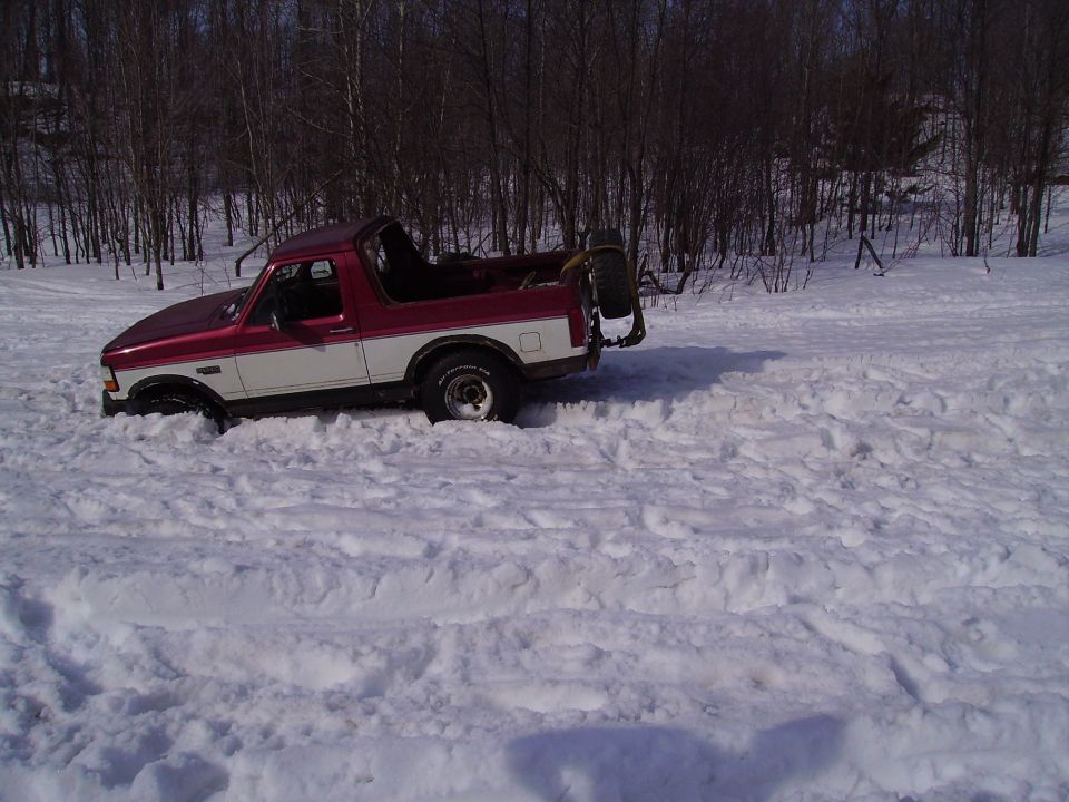 Red and white Ford Bronco stuck in deep snow, spare tire mounted on back