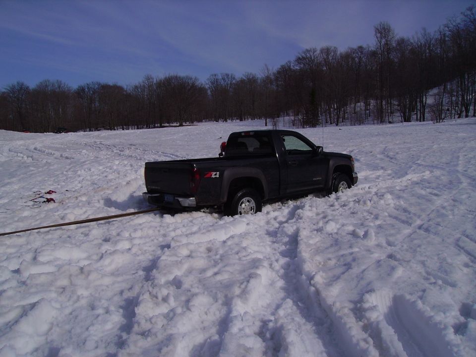 Dark gray Chevrolet Colorado pickup truck stuck in deep snow, with a tow strap attached to the rear