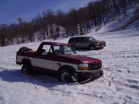 2000 Chevrolet Tahoe - Two SUVs are stuck in the snow on a wooded hillside.