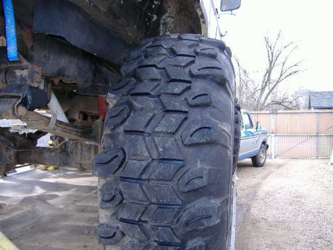 1979 Ford Bronco - A close-up view of a large off-road tire and suspension system, with a truck in the background.