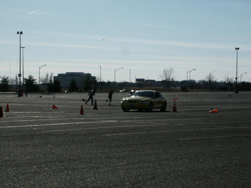 Yellow coupe with racing cones on asphalt lot. Appears to be a Ford Mustang