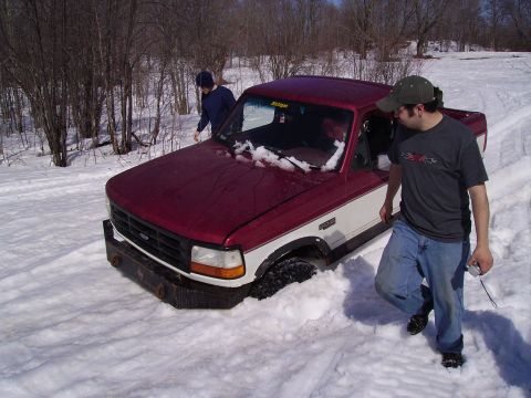 2000 Chevrolet Tahoe - Ford F-Series truck stuck in snow with two people around it.