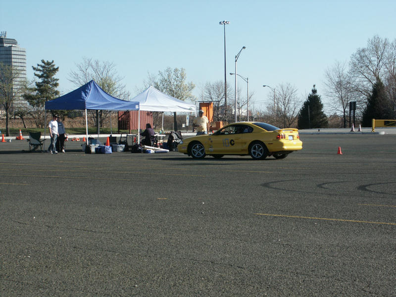 Yellow Ford Mustang with number 10C on the door, parked near tents at an event