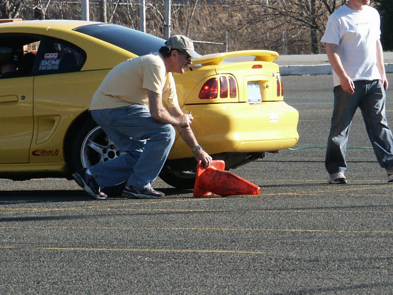 Yellow Ford Mustang Cobra with a man placing a traffic cone