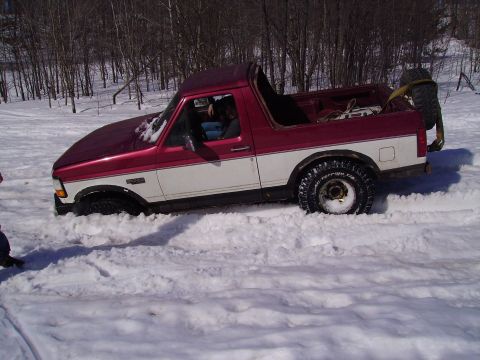 2000 Chevrolet Tahoe - A two-tone Ford Bronco is stuck in a snowy field with trees in the background.