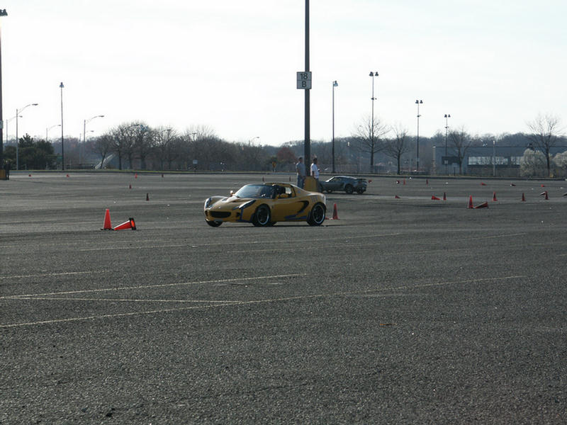Yellow sports car on asphalt course with orange cones, another car in background
