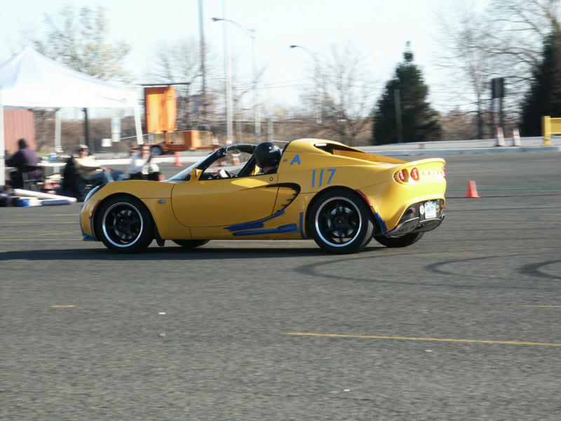 Yellow sports car with blue racing stripes and number 117 on the side, driving on asphalt