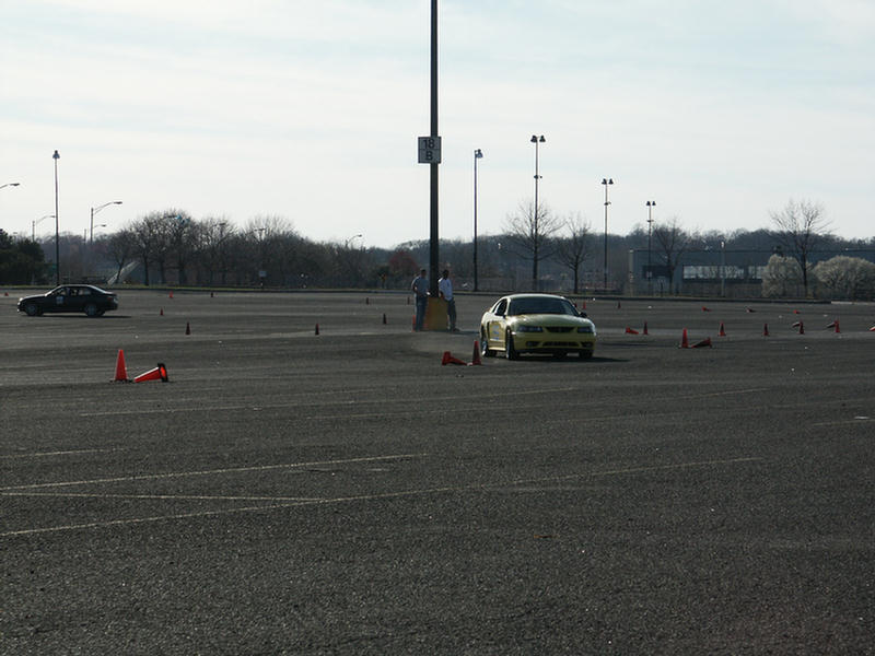 Yellow sports car navigating a cone course, another dark car in the background
